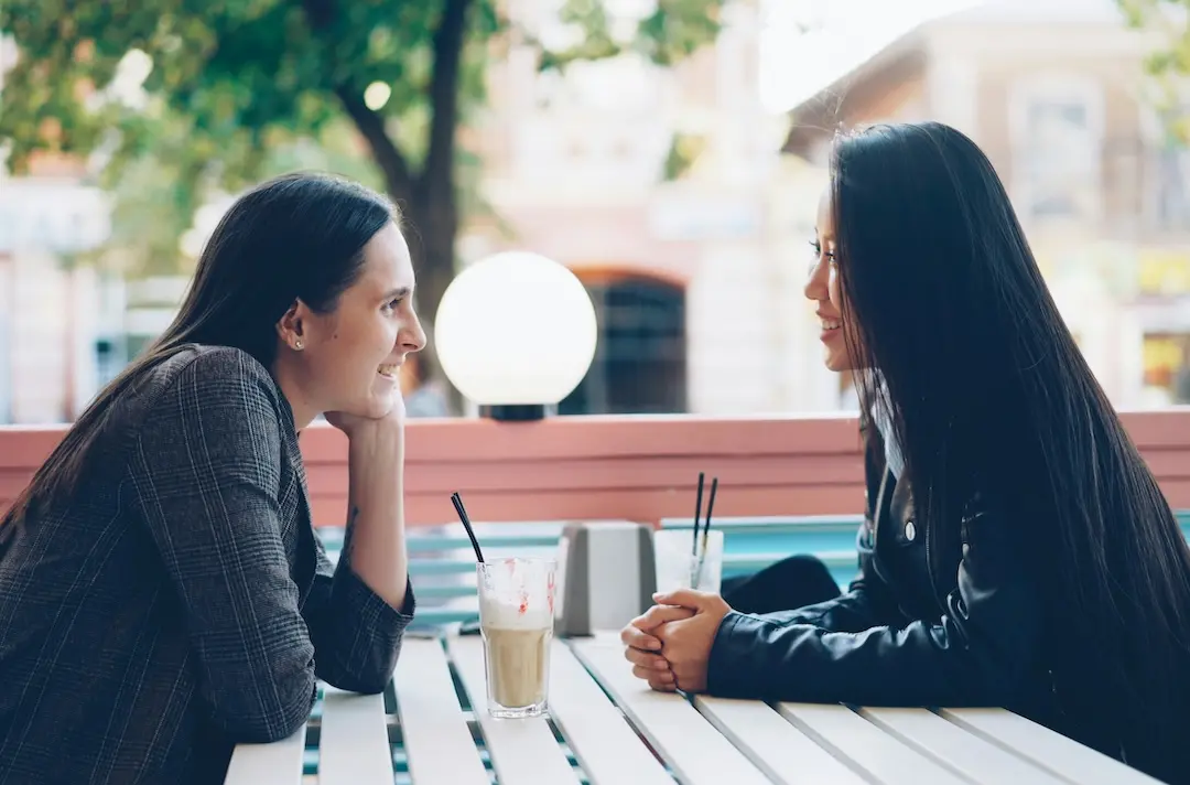 Two women sit and have a relaxed conversation at a table.
