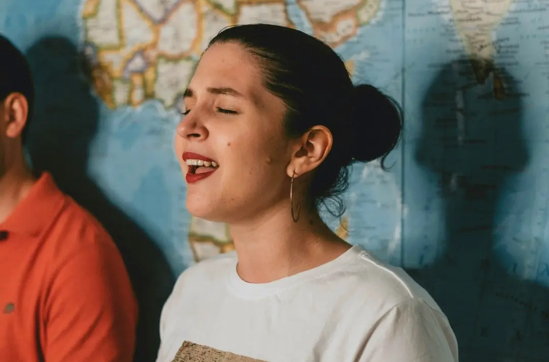 A photo shows someone singing in front of a world map.