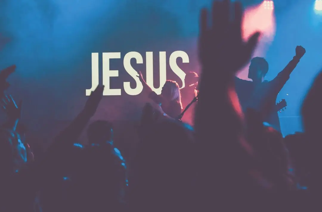 People hold their arms up in the air as they celebrate as a Christian rock concert.