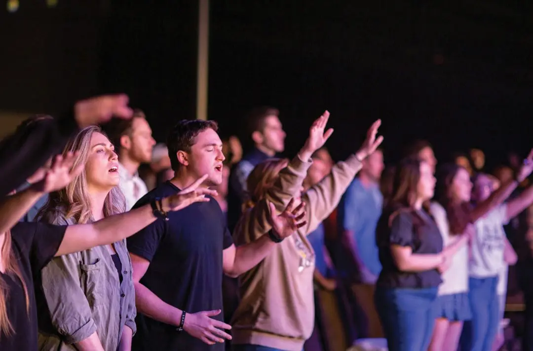 A congregation of young adults sing with their hands in the air.