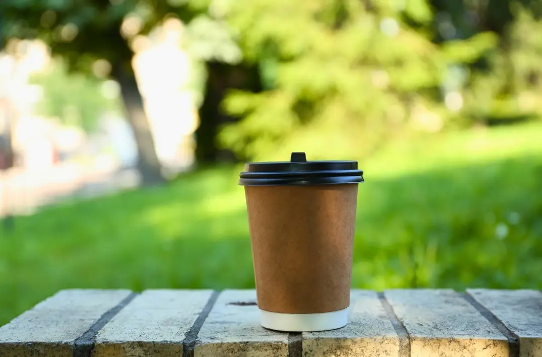A photo shows a takeaway coffee cup placed on a wall in a park.