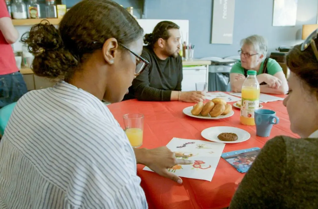 People in conversation around a table with biscuits, cakes and coffee.