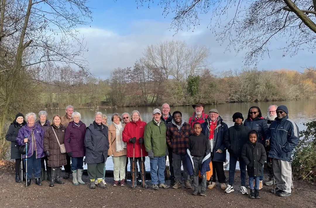 A group of people of different ages stand in front of a lake.